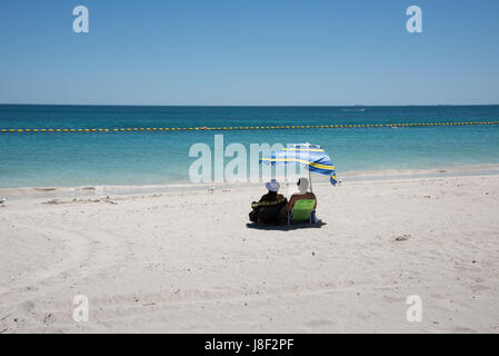 Coogee, WA, Australien-November 14,2016: Paar auf Strandliegen mit Schirm Regenschirm entspannenden mit dem indischen Ozean Seelandschaft in Coogee, Western Australia. Stockfoto