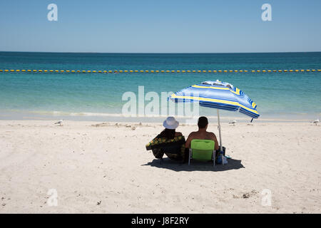 Coogee, WA, Australien-November 14,2016: Paar auf Strandliegen mit Schirm Regenschirm entspannenden mit dem indischen Ozean Seelandschaft in Coogee, Western Australia. Stockfoto