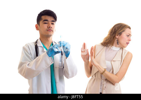 Junge Smartlooking Arzt mit schwarzen Haaren in weißes Kleid mit Stethoskop und blaue Handschuhe, die Vorbereitung für die Injektion von Angst Mädchen mit langen braunen Stockfoto