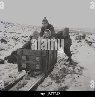 1960er-Jahren, historische, drücken Winter und zwei Väter eine alte hölzerne Minecart eine Spur mit ihren aufgeregt und etwas Angst vor kleinen Kindern sitzen drin. Stockfoto