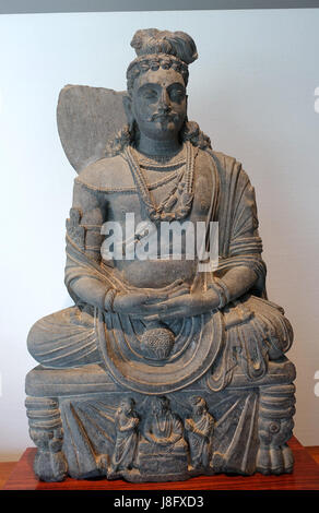 Dies ist ein Bild eines sitzenden Bodhisattva Maitreya aus Gandhara aus dem 3. Jahrhundert n. Chr. Die Skulptur ist aus grauem Schiefer geschnitzt und befindet sich im Matsuoka Museum of Art in Tokio, Japan. Maitreya repräsentiert einen zukünftigen Buddha im Mahayana-Buddhismus. Stockfoto