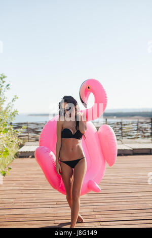 Fröhliche schöne junge tausendjährigen Frau hält bestreut rosa aufblasbare Flamingo Schwimmer im Sommer. 20er Jahre Stockfoto