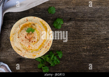 Teller mit Hummus auf Holztisch mit Serviette, Textfreiraum auf hölzernen Hintergrund, Ansicht von oben Stockfoto