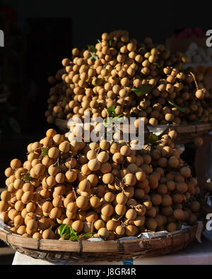 Körbe voller tropischer Longan Früchte unter Morgenlicht auf dem Straßenmarkt, Vietnam. Stockfoto