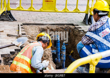 Arbeiter graben eines Lochs im Bürgersteig für Reparaturen oder Wartung Stockfoto