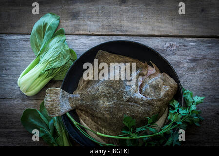 Ein Steinbutt, umgeben von jungem Gemüse; Essen; Fisch; Meeresfrüchte; Plattfische; Zutaten für eine Mahlzeit; Ungekocht; RAW; Gesunde Ernährung; Fischgericht Stockfoto