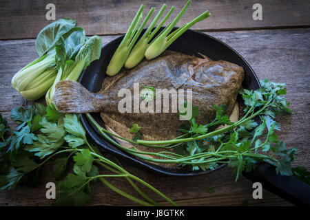 Ein Steinbutt, umgeben von jungem Gemüse; Essen; Fisch; Meeresfrüchte; Plattfische; Zutaten für eine Mahlzeit; Ungekocht; RAW; Gesunde Ernährung; Fischgericht Stockfoto
