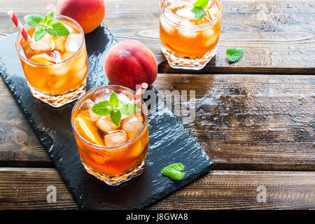 Pfirsich Eistee. Eistee mit Pfirsich Scheiben, Minze und Eiswürfel auf Schiefer und Holz rustikal Hintergrund hautnah. Hausgemachte erfrischendes Sommergetränk. Stockfoto