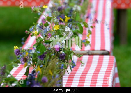 Eine Reihe von niedlichen kleinen Sommer Sträuße in Glas Gläser stehen am Anfang ein paar Tische, verziert mit roten und weißen Tischdecken. Stockfoto