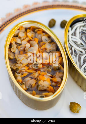 Dosen von Konserven mit Glasaale und Herzmuscheln auf einem eleganten Teller Stockfoto