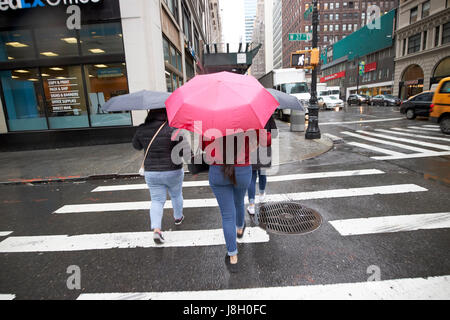 Frauen halten Sonnenschirme überqueren eine nassen Stadtstraße während Regen Dusche Midtown New York City USA Stockfoto