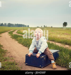 Kind sitzt auf einem Koffer Stockfoto