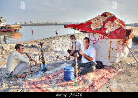 Bandar Abbas, Provinz Hormozgan, Iran - 16. April 2017: drei Männer Erholung am Strand, zwei von ihnen Rauchen einer Wasserpfeife. Stockfoto