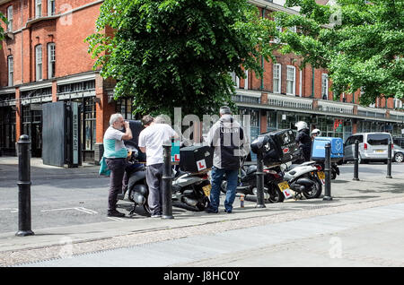 Deliveroo, Uber isst und Stuart Essen Lieferung Kuriere chatten während des Wartens auf Kundenwünsche Lieferung. Stockfoto