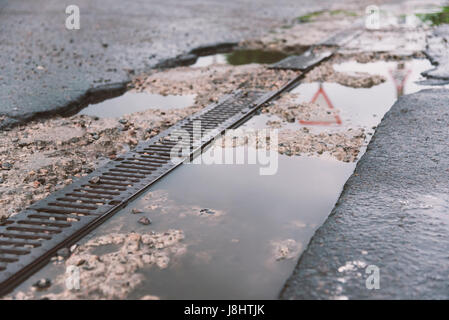 Entwässerung der Straße am Straßenrand, eine Reflexion der Umgebung im Wasser Stockfoto