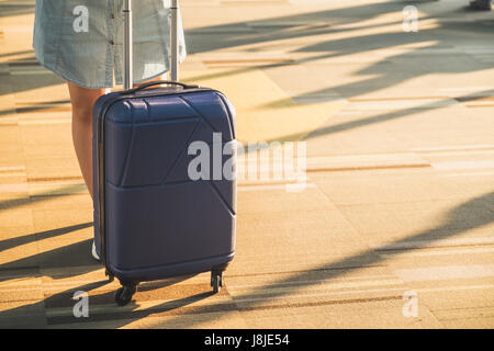 Casual Mädchen tragen weiße Turnschuhe mit Reise-Koffer mit morgendlichen Sonnenlicht durch Fenster am Flughafen terminal, Urlaub Konzept stehen. Stockfoto
