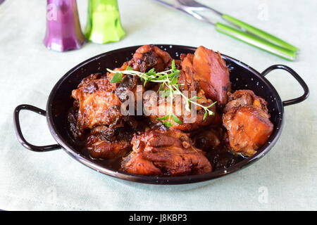 Huhn mit Pflaumen gekocht im Ofen in einer schwarzen Schale auf textilen Untergrund. Stockfoto