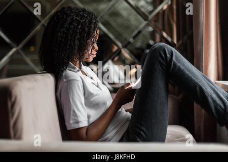 Kurze Nachricht an Freund. Attraktive junge Afrikanerin Smartphone halten und sah es beim Sitzen auf dem Sofa. Stockfoto