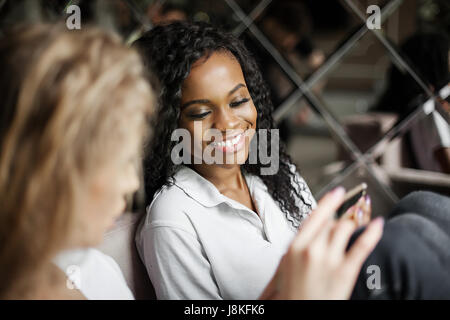 Lächelte schwarze Frau am Telefon suchen. Zwei Freunde unterhalten. Stockfoto