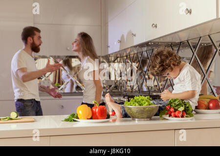 Traurig aussehende junge mit ihren kämpfen Eltern hinter ihr. Junge auf der Suche auf dem Handy-Display. Stockfoto