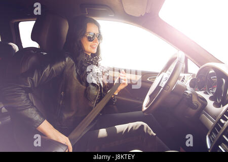 Brunette in Sonnenbrille Frau befestigt ist, mit einem Gürtel in ein teures Auto. Safety first. schönen kaukasischen lady Befestigung auto Sicherheitsgurt. Stockfoto