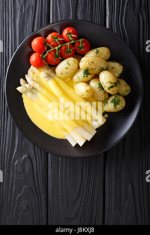 weißer Spargel mit Sauce Hollandaise, neuen Kartoffeln und Tomaten-close-up auf einem Teller auf den Tisch serviert. vertikale Ansicht von oben Stockfoto