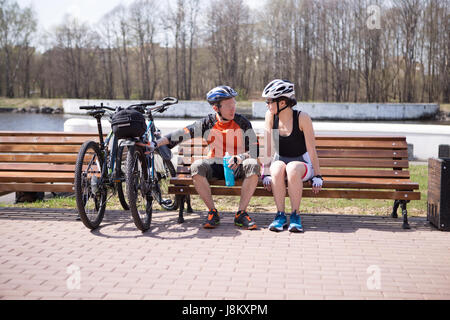 Mann mit Frau auf Bank in Helme neben Fahrrädern Stockfoto