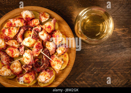 Eine obenliegende Foto von Pulpo a la Gallega, eine Krake mit gekochten Kartoffeln, typische spanische galizische Gericht, auf einer traditionellen hölzernen Platte, mit einem Glas-o Stockfoto