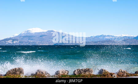 Landschaft mit einem See mit Wellen und Spritzer an einem windigen Tag, Hintergrund mit alpinen Bergwelt Stockfoto