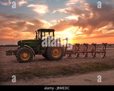 John Deere Traktor und vernetzter Pflug auf Ackerland geparkt mit echtem goldenen Himmel über dem Sonnenuntergang oder Sonnenaufgang, wenn Sie Essex England möchten Stockfoto