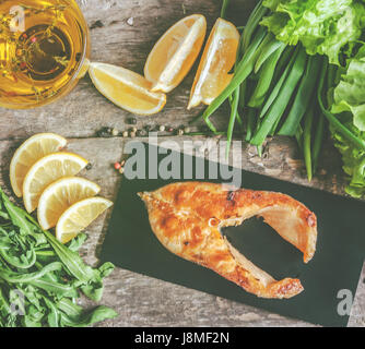 Gebackene Steak Forelle Fisch auf einer Steinplatte, um grünen, Blätter, Salat, Zitrone, Olivenöl, Pfeffer, Gewürze. Von oben, close-up, retro, Vintage ef Stockfoto