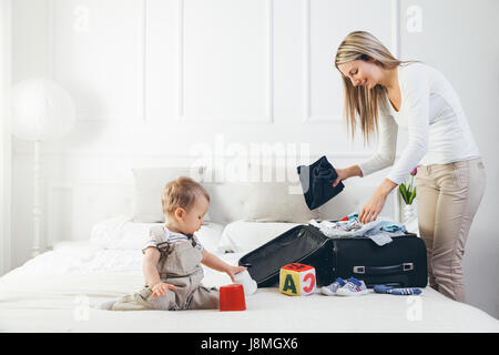 Reisen mit Kindern. Glückliche Mutter mit ihrem Kind Verpackung Kleidung für ihren Urlaub Stockfoto