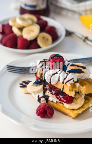 Belgische Waffeln mit Himbeeren und Bananen auf weißen Teller und weißem Hintergrund. Stockfoto