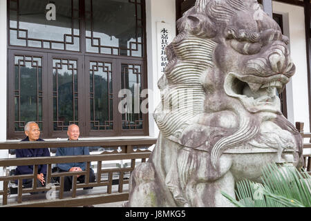 Yubei, Zhejiang, China.  Zwei ältere Herren auf Veranda mit Guardian Lion (Shi oder Foo Dog) im Vordergrund. Stockfoto