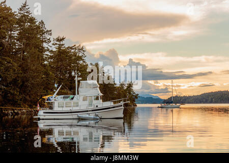 Zwei Boote (a Nordic Tug und ein Segelboot) sind bei Sonnenuntergang auf einem ruhigen Abend an einem Marine Park in British Columbia Gulf Islands verankert. Stockfoto