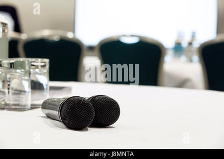 Zwei Mikrofone auf einen weißen Tisch, einer Konferenz oder Tagung Veranstaltungsort für Q&A verwendet. Stühle und einen Bildschirm im Hintergrund Stockfoto