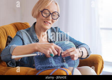 Im Prozess. Porträt der aufmerksame Blonde Lächeln auf ihrem Gesicht zu halten und beim stricken eine Runde Brille Stockfoto