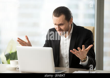Verärgert schockiert Geschäftsmann am Bürotisch befasst sich mit Laptop-Bildschirm mit überrascht verwirrten Ausdruck, Finanzdaten verloren. Emotionale Büro Arbeiter Don t Stockfoto