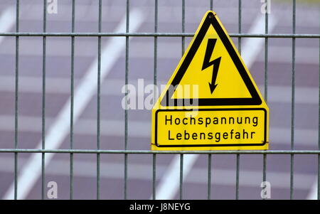 Melden Sie mit den Worten Hochspannung - Lebensgefahr in deutscher Sprache vor Sonnenkollektoren. Stockfoto