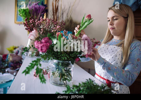 Frau Florist Blumenstrauss indoor machen. Weibliche Vorbereitung Blumenstrauß mit Rosen, Pfingstrosen und Tulpen im Blumenladen Blumengeschäft Stockfoto