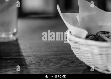 Brotscheiben in den Korb und ein Glas Wasser mit unscharfen Holztisch Hintergrund. Schwarz und weiß. Stockfoto
