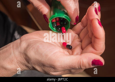 Frauen nehmen Sie rote und schwarze Kapsel mit rechten Hand aus einer grünen Flasche auf schwarzem Hintergrund Stockfoto