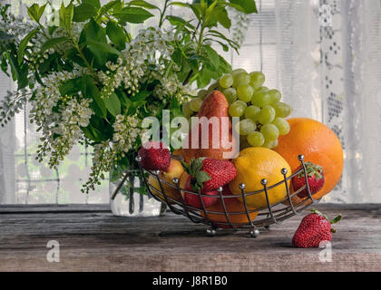 Frucht, Birne, Grapefruit, Zitrone, Pfirsich, Erdbeeren in einem Korb auf dem Hintergrund ein Bouquet von kleinen weißen Blüten an einem sonnigen Tag sind. Die horizontalen Rahmen. Stockfoto