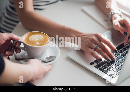Nahaufnahme Bild von Händen der Kellner geben eine Tasse Cuppuccino, einer Frau mit einer Tastatur tippen. Stockfoto