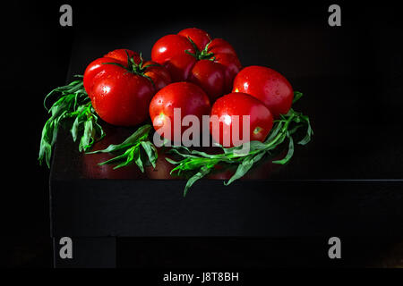 Drei große frische Tomaten. Zweige Estragon und Wasser Tropfen auf einem dunklen Hintergrund aus Holz Stockfoto