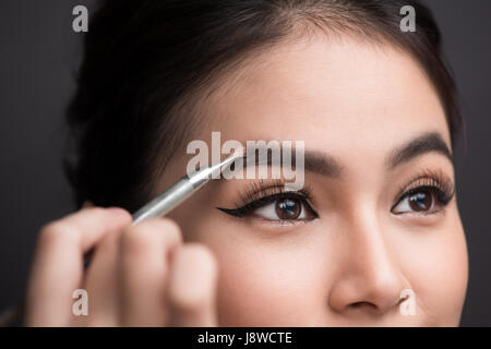 Nahaufnahme des schönen Gesicht der jungen Asiatin immer Make-up. Der Künstler setzt Lidschatten auf ihre Augenbrauen mit Pinsel Stockfoto