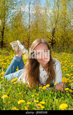 Junge Frau liegt in einem Feld von Löwenzahn, vor einem Birkenwald, Ystad, Scania, Schweden Stockfoto