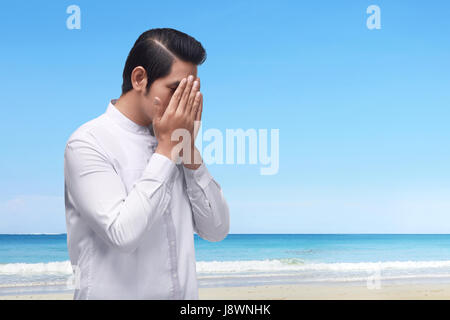 Porträt von asiatischen muslimischen Mann in traditioneller Kleidung mit blauen Skyline Hintergrund beten Stockfoto