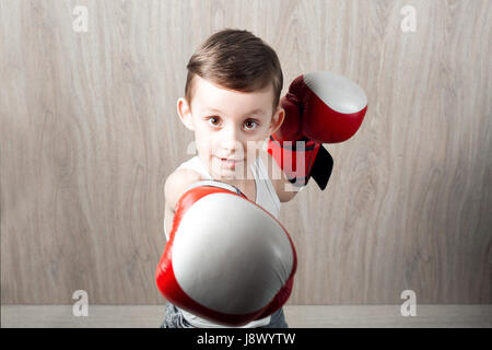 niedliche kleine Junge mit Größe Boxhandschuhe. Porträt eines sportlichen Kindes engagiert im Feld. Narren um und nicht ernst. hölzerne Hintergrund Stockfoto