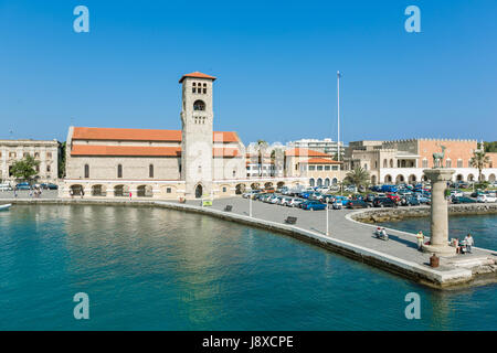 Rhodos, Griechenland - 12. Juni 2015: Aussicht auf eine Mandaki Hafen Hafen und einem Damm mit einer Kapelle und die Statue des Hirsches. Menschen zu Fuß auf einem Damm beobachten Stockfoto